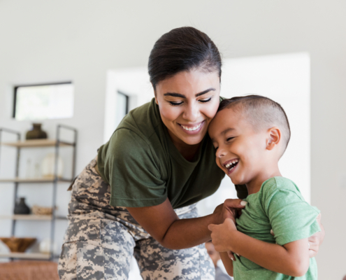 military woman embracing her laughing young son, highlighting support for children during deployment.
