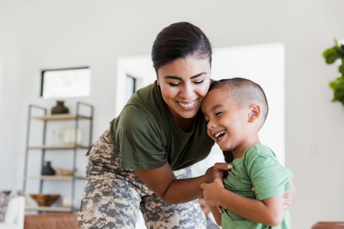 military woman embracing her laughing young son, highlighting support for children during deployment.