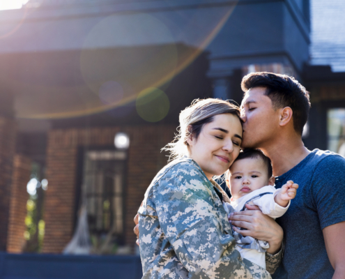 military spouse in uniform embracing her baby, husband kisses her forehead, support for military families