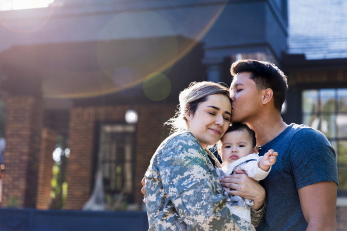 military spouse in uniform embracing her baby, husband kisses her forehead, support for military families