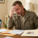 stressed veteran looking at veteran financial assistance forms with a laptop showing spreadsheets.