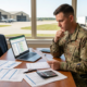 a uniformed military member reviewing documents at a desk, laptop visible with a spreadsheet, suggesting military transition planning.