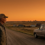 veteran in cap gazing at rural landscape with truck and distant town at sunset, highlighting rural veteran services