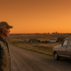 veteran in cap gazing at rural landscape with truck and distant town at sunset, highlighting rural veteran services