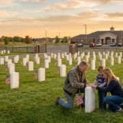 family kneels at a veteran's tombstone in a cemetery during sunset, emphasizing veteran emergency support.