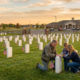 family kneels at a veteran's tombstone in a cemetery during sunset, emphasizing veteran emergency support.