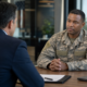 a veteran in uniform speaking to a man in a suit about veteran employment programs.