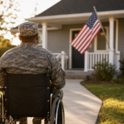 disabled veteran in camouflage uniform in a wheelchair facing a house with an american flag, representing veteran housing rights