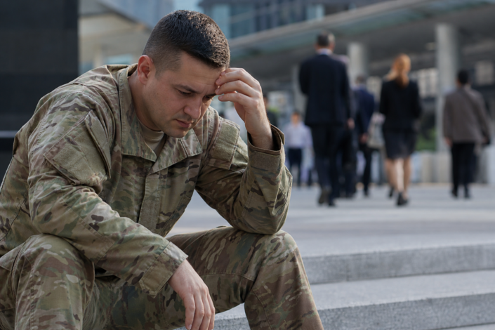 distressed soldier in camouflage uniform, hand on forehead, contemplating military transition employment barriers.