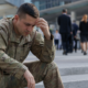 distressed soldier in camouflage uniform, hand on forehead, contemplating military transition employment barriers.