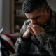 distressed veteran in uniform, hands clasped, indicating at-risk veterans warning signs; flag and crutches behind him.