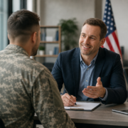 smiling man in suit helping a veteran in uniform with unemployed veterans programs paperwork.