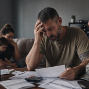distressed veteran reviewing bills, facing economic hardship, with worried family in background.