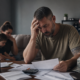 distressed veteran reviewing bills, facing economic hardship, with worried family in background.