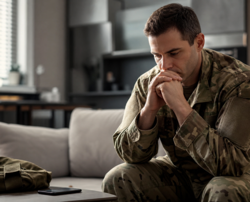 distressed man in military fatigues on couch, considering early intervention veteran housing